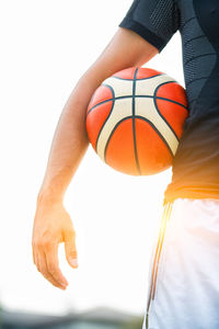 Midsection of man with basketball on waist against sunbeam