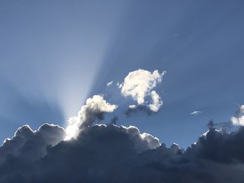 Low angle view of sunlight streaming through clouds