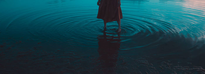 Low section of woman standing in sea during sunset