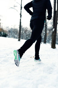 Low section of woman running on snow covered field