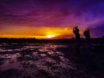 Silhouette friends standing against sky during sunset