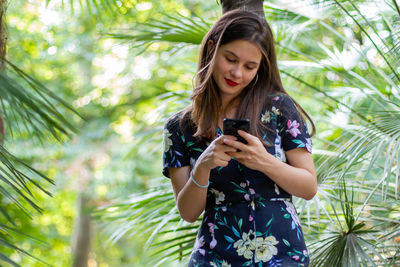 Young woman using mobile phone while standing on tree