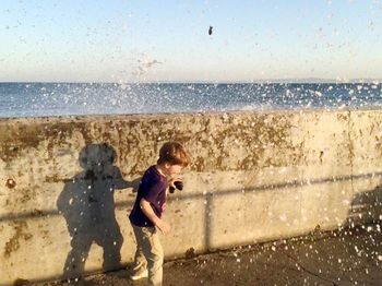 Water splashing on boy standing by retaining wall