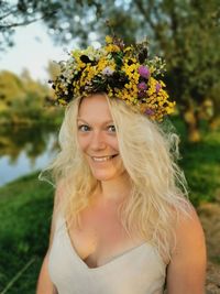 Portrait of happy woman wearing flowers while standing at park