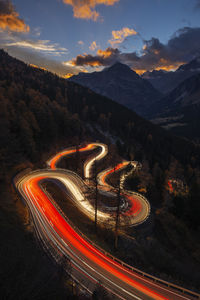 Switzerland, grisons, sankt moritz, vehicle light trails stretching along maloja pass road at dusk