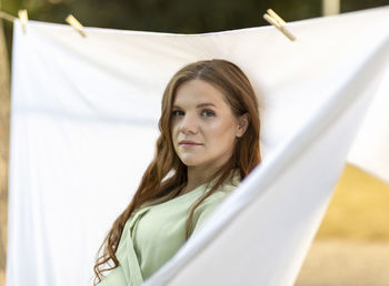 Pretty white pregnant woman hanging up laundry on clothes line outside, drying bed linens, bedding