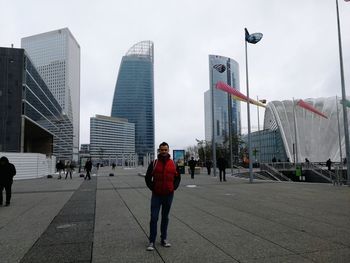 Man walking on street by buildings against sky in city