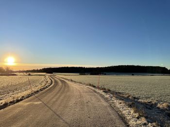 Road amidst land against clear sky during sunset