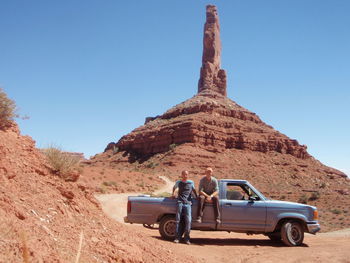 Men relaxing by pick-up truck against rock formation
