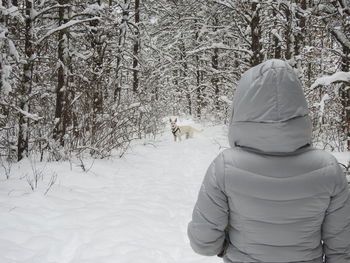 Rear view of woman with dog walking in forest during winter