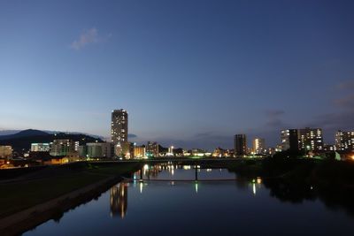 River by illuminated buildings against sky at night