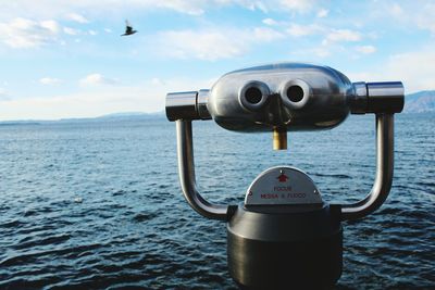 Close-up of coin-operated binoculars by sea against sky