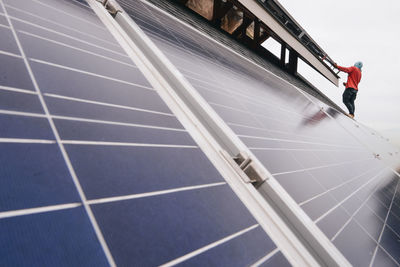 Low angle view of man installing solar panel against sky