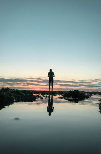 Silhouette man standing on shore against sky during sunset