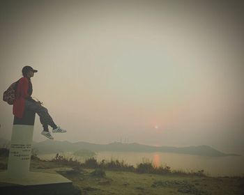 Side view of man standing on field against sky during sunset