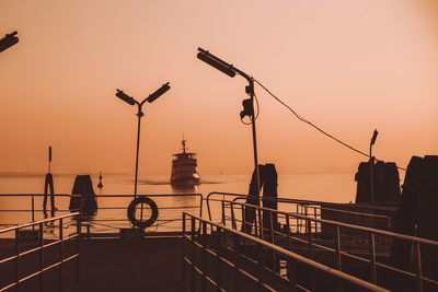 Silhouette street light against boat in sea during sunset