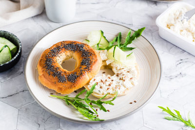 Bagel sandwich with cream cheese, cucumber and arugula on a plate on the table. homemade breakfast