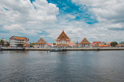 View of buildings by river against cloudy sky