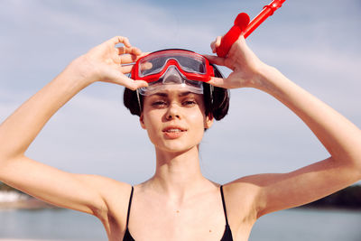 Portrait of young woman with arms raised standing against sky