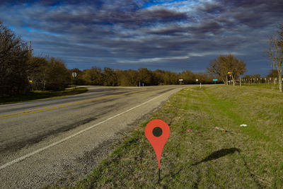 Pointer stick on grassy field by empty road against sky