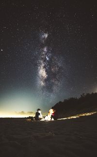 People sitting on sand against sky at night