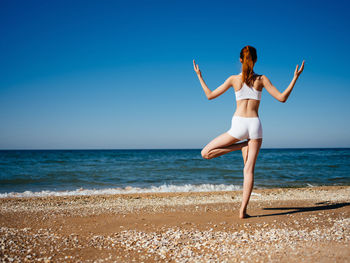 Full length of young woman at beach against clear sky