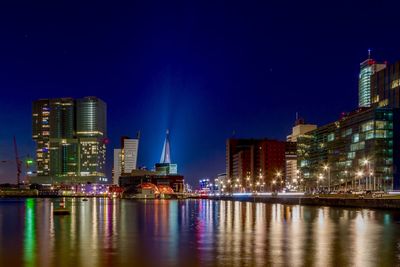 Illuminated buildings by river against sky at night