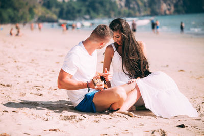 Young man playing ukulele while sitting with girlfriend at beach