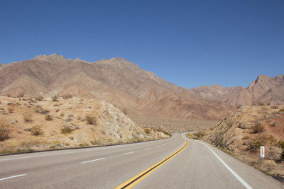 Road leading towards mountains against clear blue sky