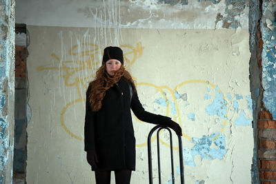 Portrait of young woman standing against abandoned wall