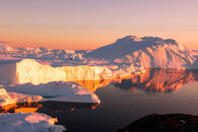 Scenic view of lake by snowcapped mountains against sky during sunset