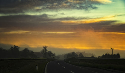 Road by field against sky during sunset