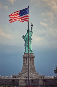 Low angle view of flag against statue and sky