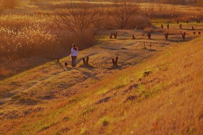 Rear view of woman with dog running on grassy field at morning