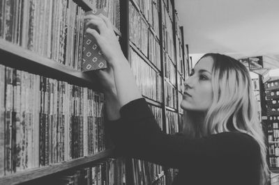 Side view of young woman searching book in shelf at library