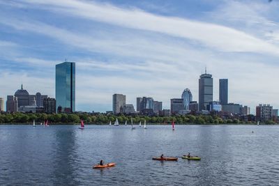 Boats in river by buildings in city against sky