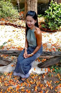 Full length of smiling young woman sitting on autumn leaves