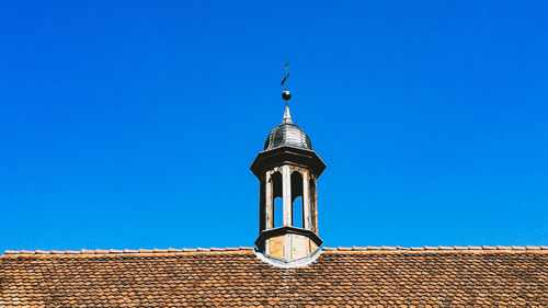 Low angle view of cross on roof of building against clear blue sky