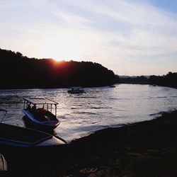 Boat moored on lake against sky during sunset