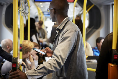 Side view of male commuter standing with mobile phone in bus