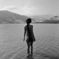 Rear view of naked woman standing in lake