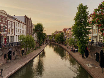 Canal amidst buildings in city against sky at sunset