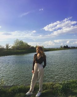 Young woman standing by lake against sky