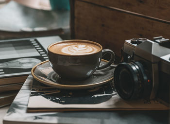 Cup of coffee with latte art on books next to vintage film camera