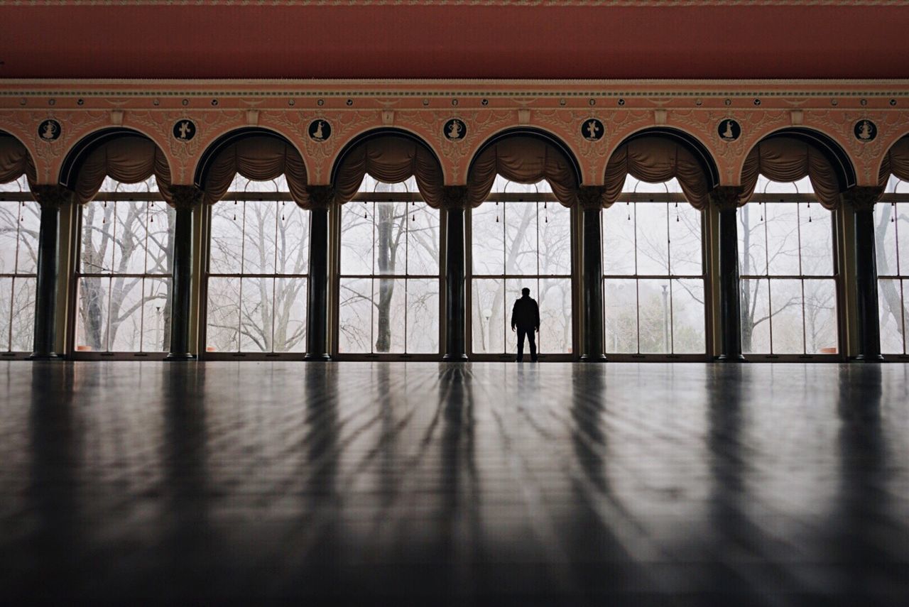 indoors, window, architecture, built structure, glass - material, silhouette, reflection, transparent, arch, flooring, men, lifestyles, copy space, day, standing, in a row, building, person