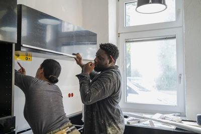 Diverse male and female carpenters working together in kitchen at apartment