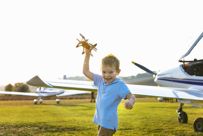 Cute little boy playing with toy plane while standing at airfield