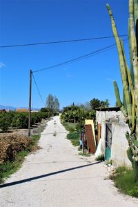 Dirt road by footpath against clear blue sky