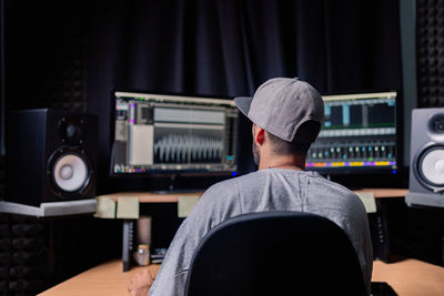 Back view of unrecognizable male musician sitting at table with monitors and stereo speakers while recording audio in studio