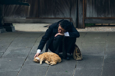 Businessman crouching by cat on footpath